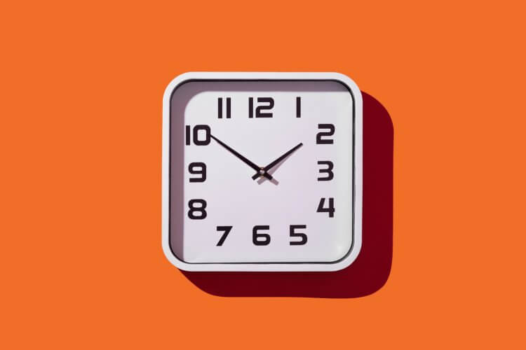 an illustrative image of a clock on a solid orange background used as a header image for Slido's blog about how to design a great all-hands meeting agenda